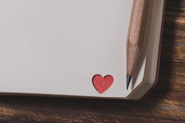 Free Photo corner of a notebook with a red heart and a pencil