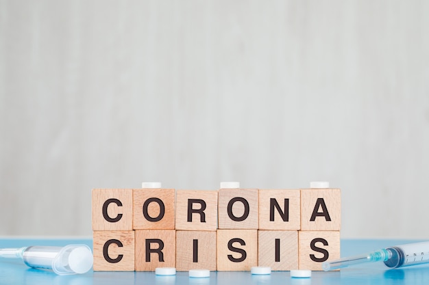 Coronavirus crisis concept with wooden cubes, medical pills, syringe on blue and grey table side view.