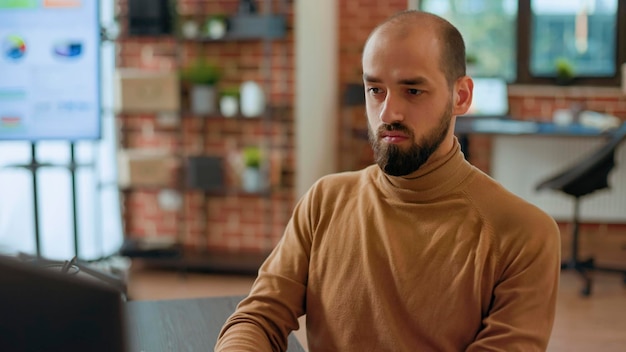 Corporate employee working with statistics and financial charts on computer, looking at documents with project plan. Professional businessman analyzing management strategy for company growth.