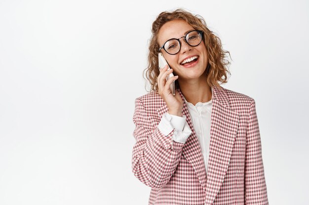 Corporate female manager answering phone call, smiling while using cellphone, having conversation, standing over white background