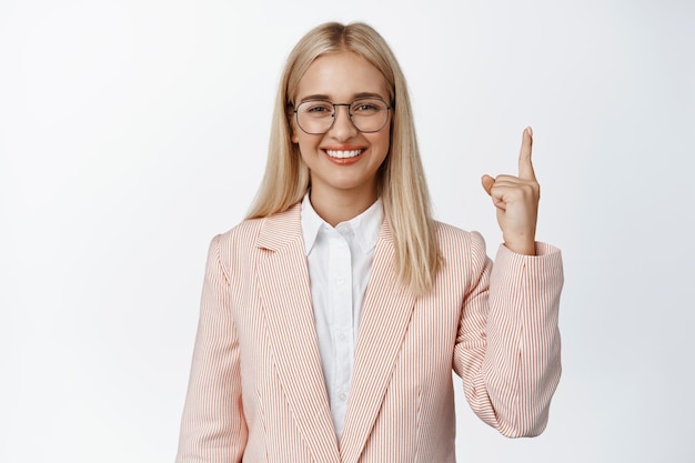 Corporate people Professional saleswoman in suit and glasses smiling pointing finger up showing advertisement white background