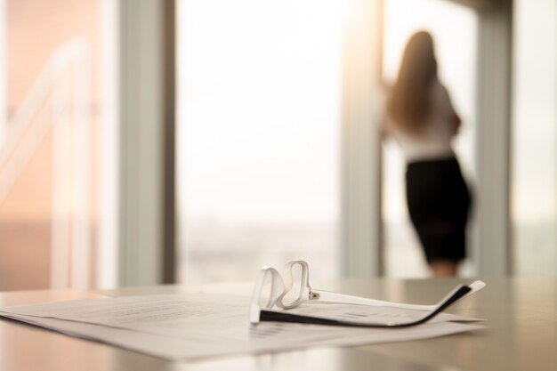 Corrective glasses for reading on desk, female silhouette at background