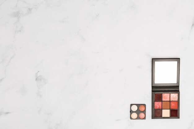 Cosmetic makeup eye-shadow and face powder palette on the corner of the white textured backdrop