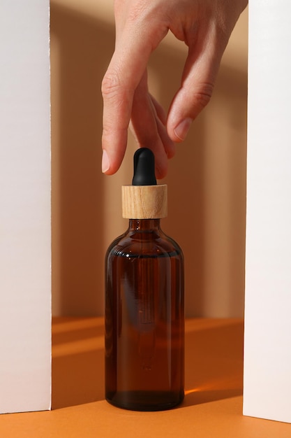 Free Photo cosmetic serum bottle and hand on orange background