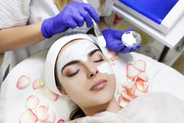 Free photo cosmetologist applies white mask on woman's face