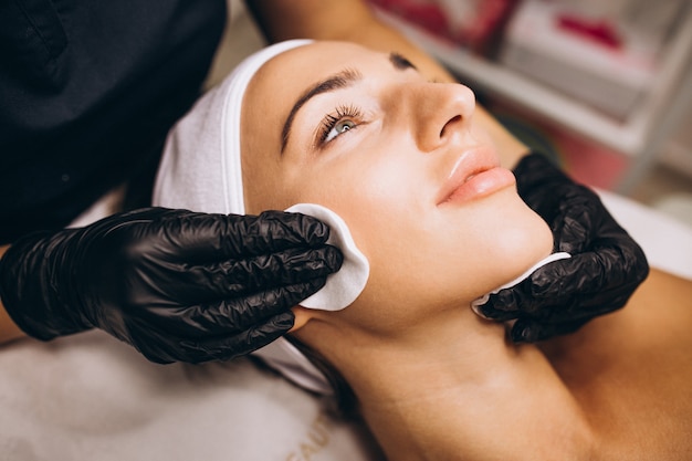 Cosmetologist cleaning face of a woman in a beauty salon