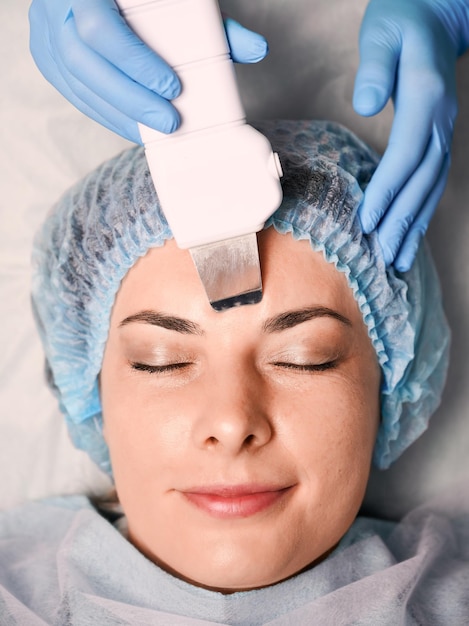 Cosmetologist cleaning woman forehead with ultrasonic scrubber