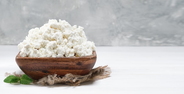 Cottage cheese in a traditional wooden bowl on a white wooden background. Close-up, selective focus with copy space. Soft curd natural healthy food, wholesome diet food