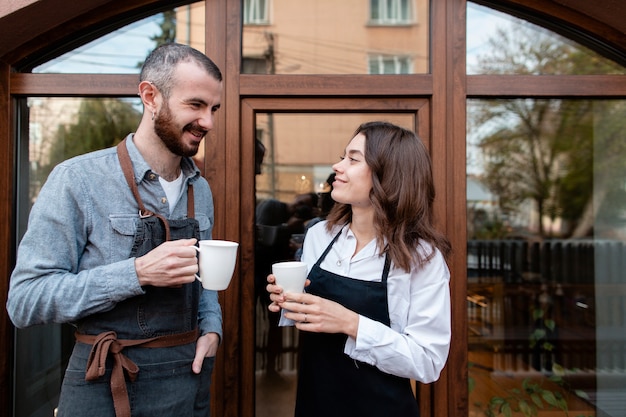 Free photo couple in aprons enjoying coffee outside shop