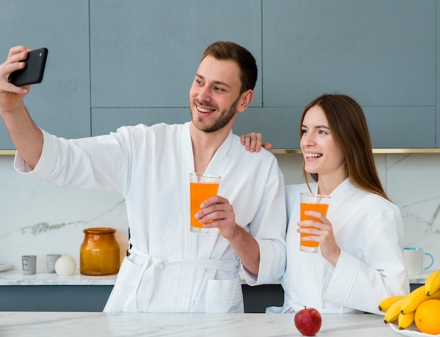 Couple in bathrobes taking a selfie with glasses of juice