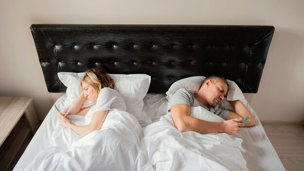 Couple in bed back to back using mobiles