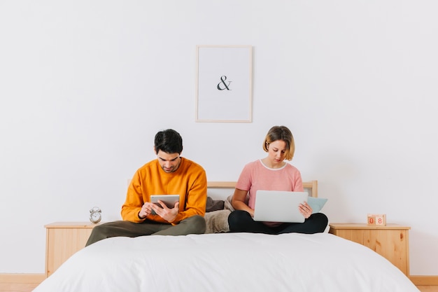 Free Photo couple browsing laptop and tablet on bed