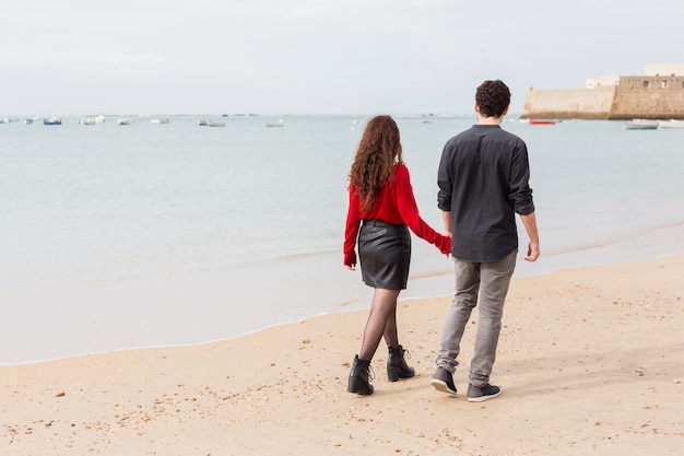 Couple in casual clothes walking on sea shore