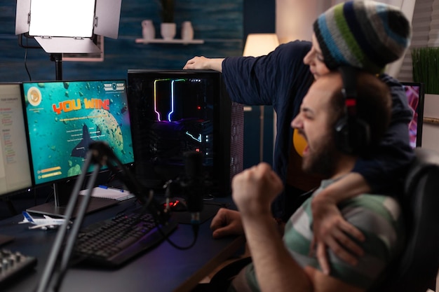 Free photo couple celebrating video games win on live stream. woman feeling happy about man winning gameplay while he is streaming online with chat on computer. streamer using gaming equipment