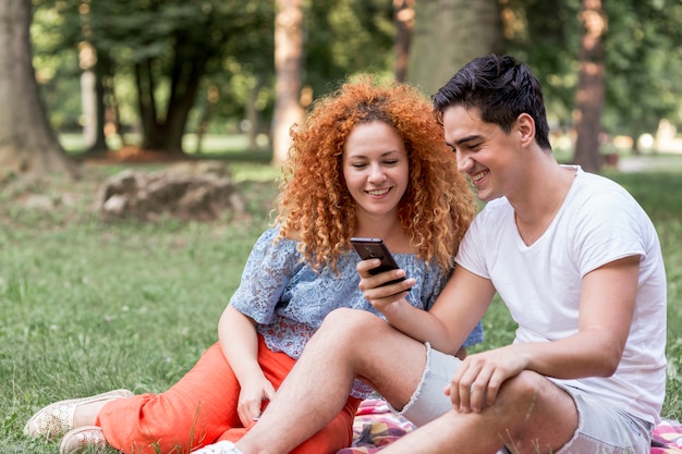 Free photo couple checking cell phone in the park and having fun