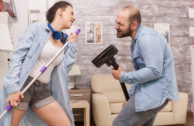 Couple cleaning house and singing on vacuum cleaner