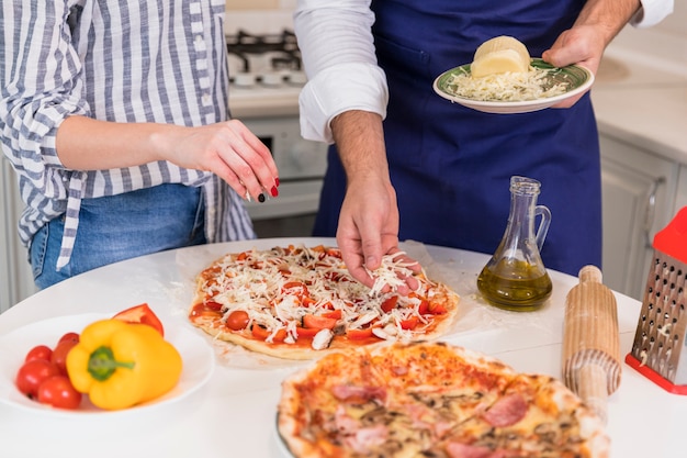 Free photo couple cooking pizza with cheese at table