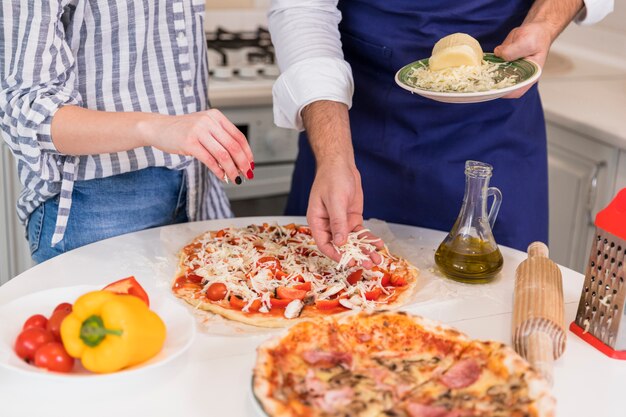 Couple cooking pizza with cheese at table