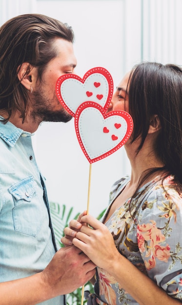 Free Photo couple covering faces with paper hearts on stick