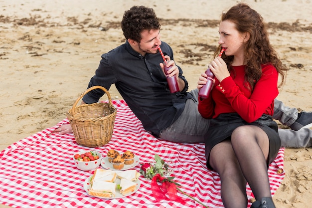 Couple drinking from bottles on checkered coverlet 