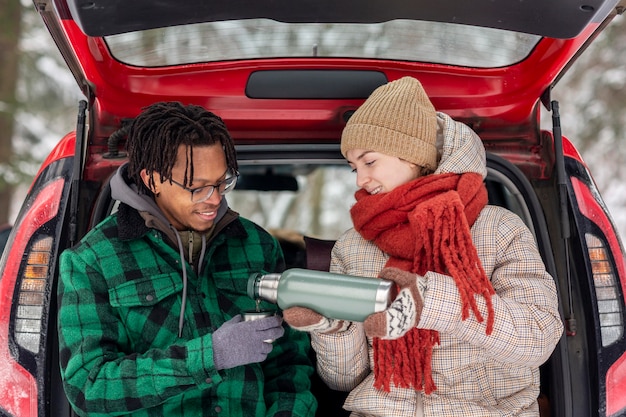 Couple drinking tea while sitting on car trunk