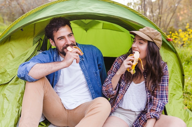 Free Photo couple eating bananas near tent