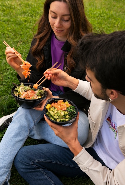 Couple eating bowl of salmon on the grass outdoors