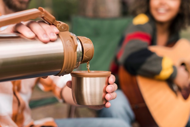 Couple enjoying camping outdoors with guitar and hot drink