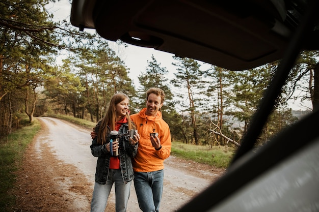 Free photo couple enjoying hot beverage while on a road trip with the car