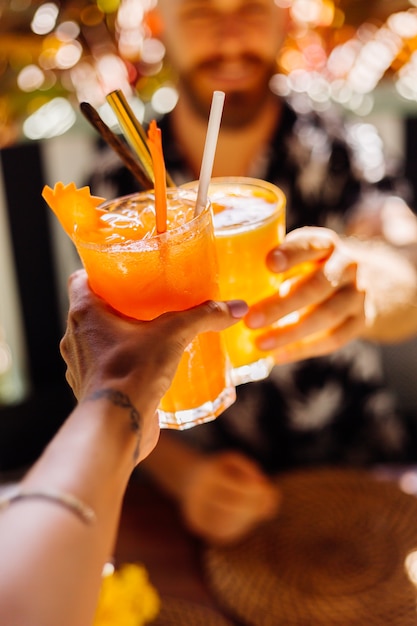 Couple friends clinking glasses of tasty tropical cocktails on sunny day in cafe