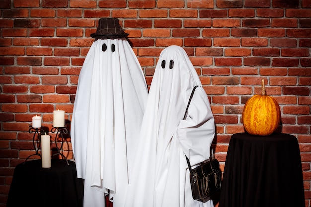 Couple of ghosts posing over brick wall Halloween party.