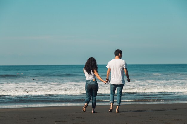 Couple going barefoot on sand to sea