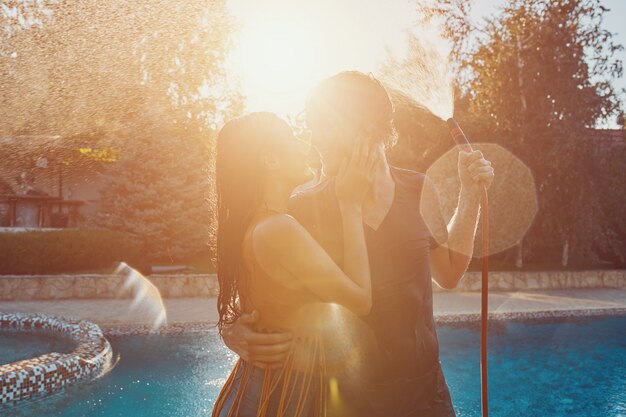 Couple having fun pour each other with garden hose