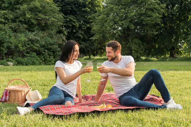 Couple having orange juice on picnic blanket