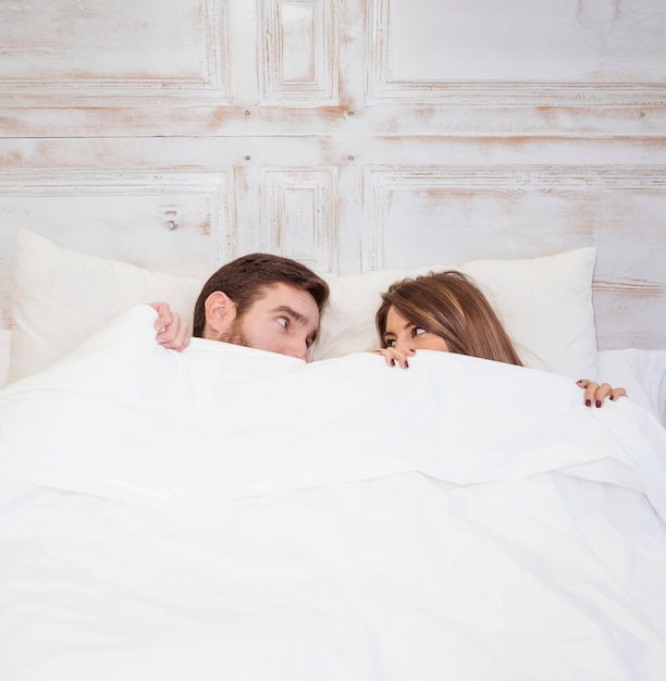 Couple hiding under blanket on bed 