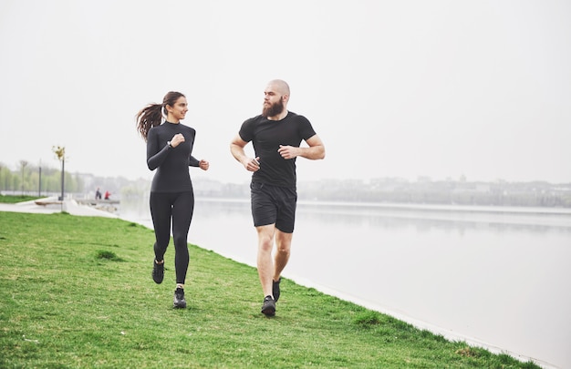 Free photo couple jogging and running outdoors in park near the water. young bearded man and woman exercising together in morning