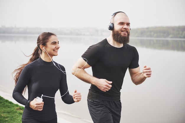 Couple jogging and running outdoors in park near the water. Young bearded man and woman exercising together in morning