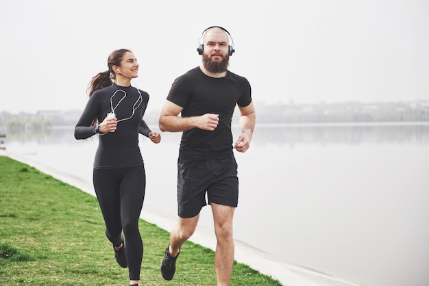 Free photo couple jogging and running outdoors in park near the water. young bearded man and woman exercising together in morning