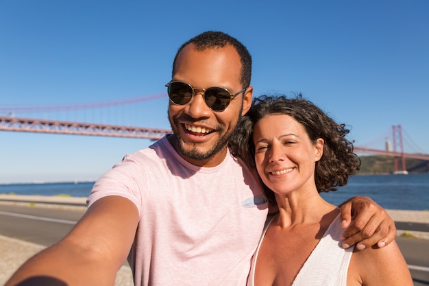 Couple of joyful tourists taking selfie on city promenade