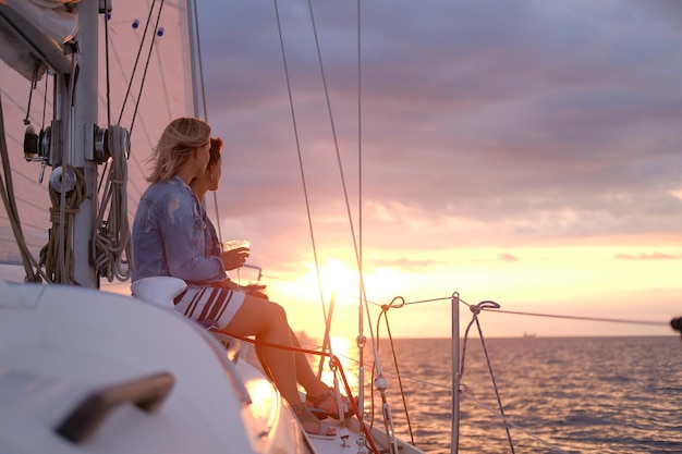 Free Photo couple of ladies are enjoying their trip on sailing boat while drinking wine and watching beautiful sunset.