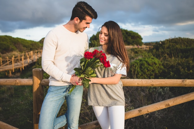 Couple leaning on a railing of a bridge with a bouquet of roses