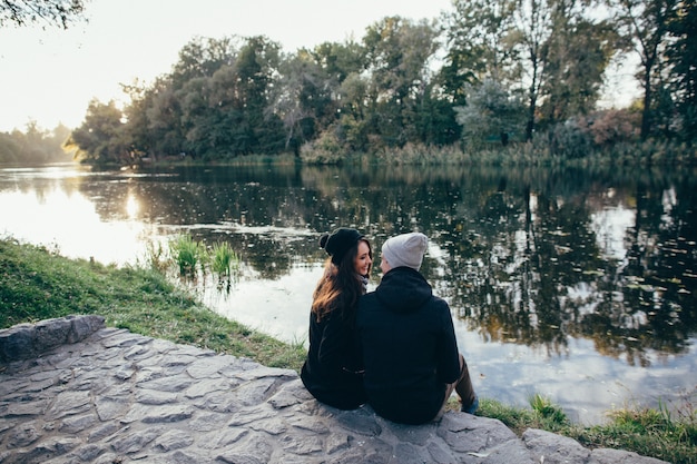 Free Photo couple in love. beautiful couple in love in warm clothes sits on riverside at sunset.