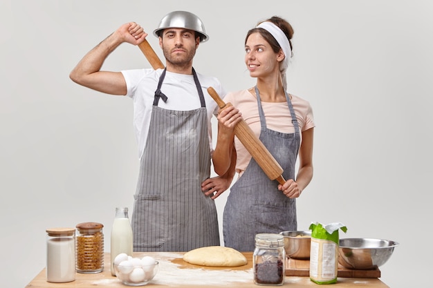 Couple in love busy with family cooking, stand self assured at kitchen, make dough for preparing pie, have all needed ingredients, hold rolling pin, prepare for party. Food, cooking, recipe concept