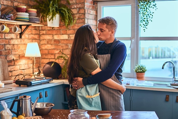 Couple in love. Handsome male embrace and kiss his wife in loft style kitchen at morning.