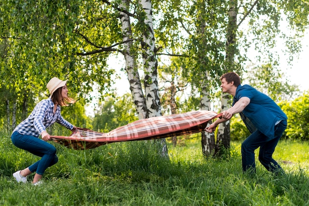 Free photo couple in love placing picnic blanket on meadow