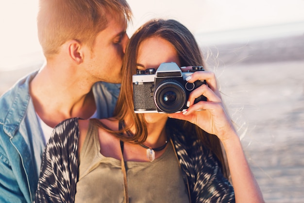 Free photo couple in love posing on the  evening beach, young hipster girl and her handsome boyfriend taking photos with retro film camera. sunset warm light.