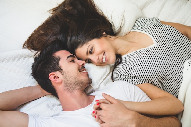 Couple lying on the bed holding hands and looking into each other's eyes