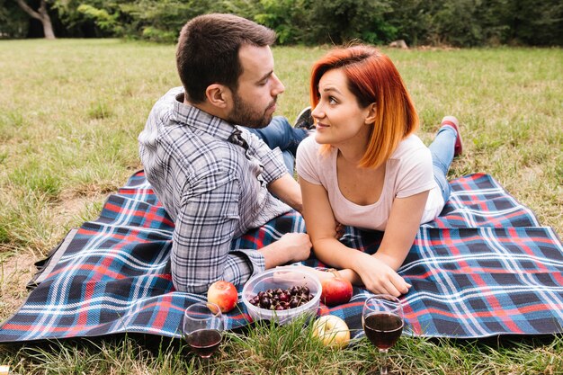 Couple lying on blanket over green grass enjoying fruits