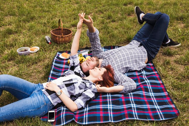 Couple lying on blanket over green grass holding each other's hand on picnic