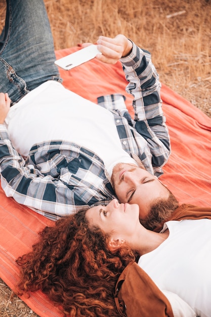 Free Photo couple lying on blanket taking a selfie